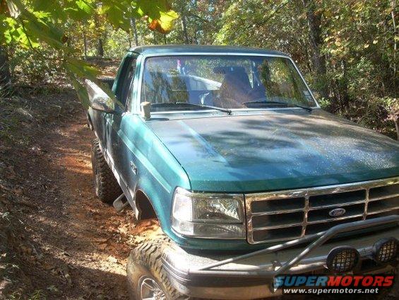 Green 1992 Ford F-150 pickup truck with off-road tires on a dirt trail