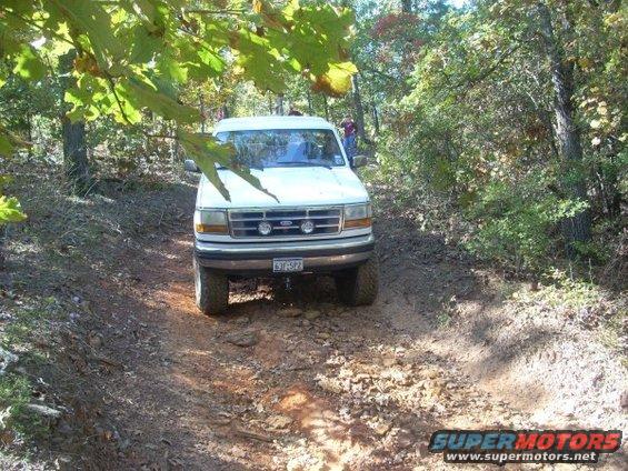 White 1992 Ford Bronco on a dirt road, front view, with trees and foliage