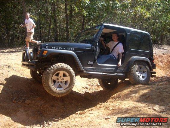 Black Jeep Wrangler Rubicon on a dirt trail with a man driving and another running behind