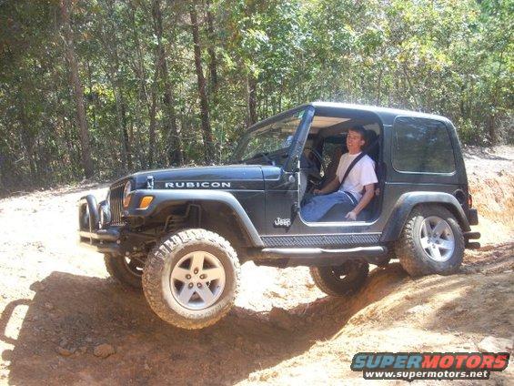 Black Jeep Wrangler Rubicon with a person driving off-road on a dirt path