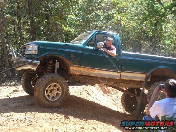 Green lifted pickup truck driving on a dirt trail with a man in the driver's seat and another person taking a photo
