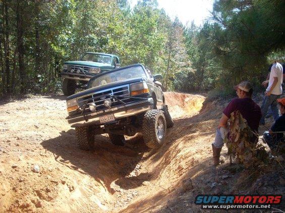 1992 Ford Bronco navigating a steep dirt rut with another truck behind it