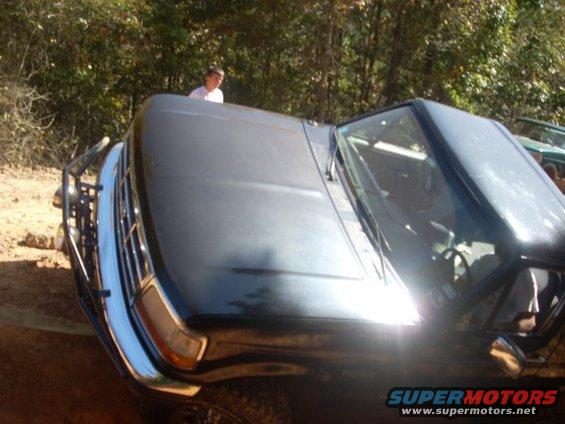 Dark-colored 1992 Ford Bronco tilted on its side, front grille and bumper visible, with a person standing behind it