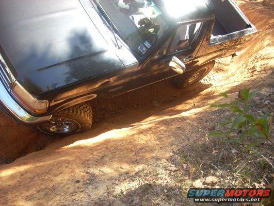 1992 Ford Bronco driving on a dirt trail, front wheel deep in a rut