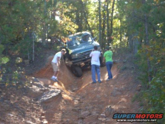 Off-road vehicle navigating a steep dirt trail with three people watching