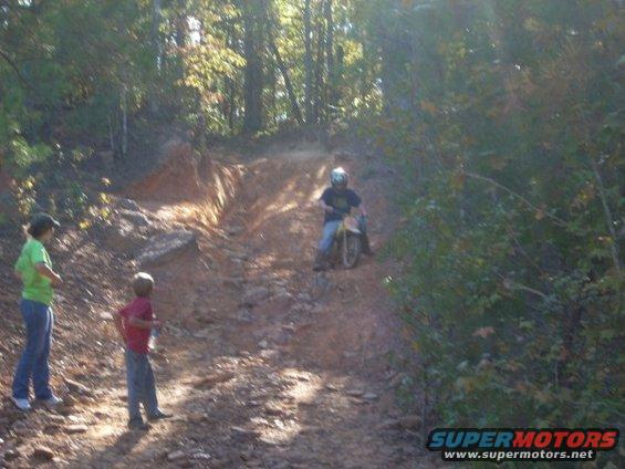 Kid on dirt bike going up a hill, two kids watching