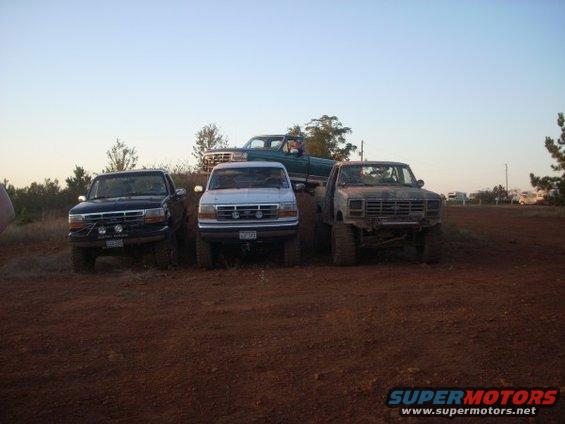 Three Ford trucks and one green pickup truck parked on a dirt hill