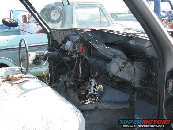 Disassembled interior of a light blue pickup truck, showing exposed wiring and steering column. Another truck is visible in the background
