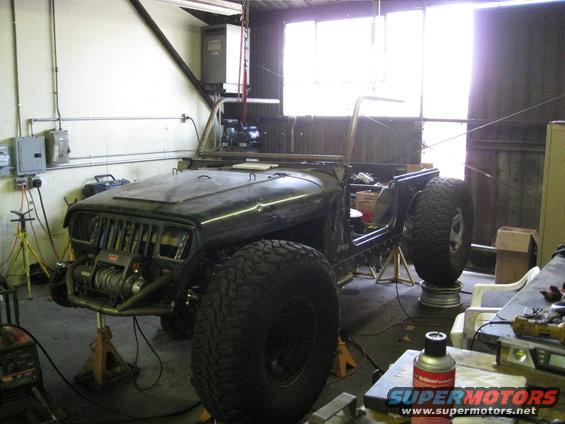 Dark green Jeep Wrangler body on jack stands, missing doors and windshield, with a winch on the front bumper