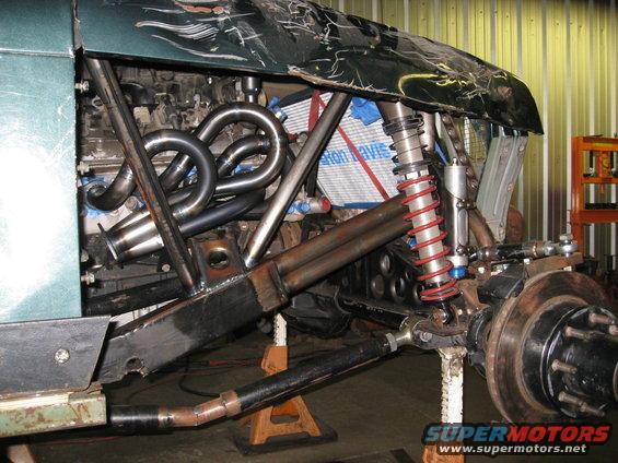 Custom off-road vehicle suspension with headers and engine components visible. Vehicle is on jack stands