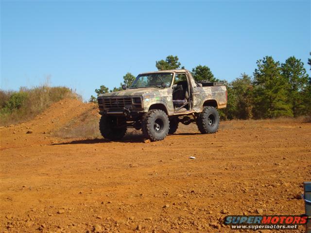 Camouflaged pickup truck with lifted suspension and large tires parked on dirt