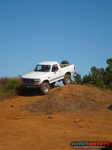 White pickup truck climbing a dirt hill with a spare tire in the bed