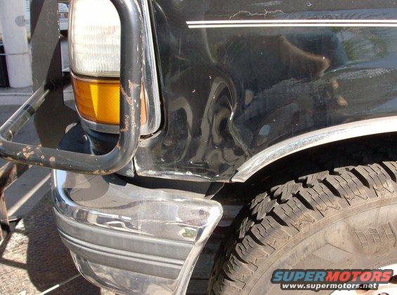close-up of dented black SUV fender and chrome bumper