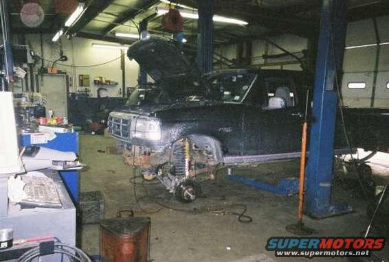 Black Ford truck with hood open, undergoing repairs on a lift. Front grille and headlights are visible