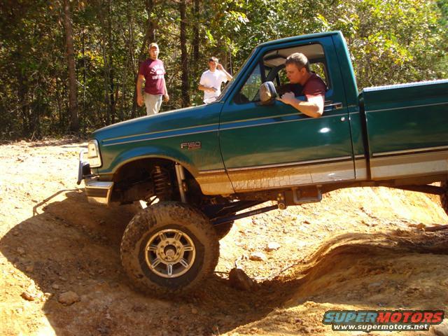 Green pickup truck with lifted suspension navigating a dirt trail