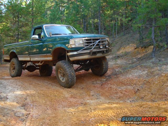 Green pickup truck with lifted suspension and off-road tires on a dirt trail