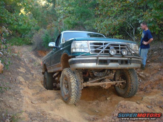 Green lifted pickup truck on a dirt trail, front view. Likely 1992