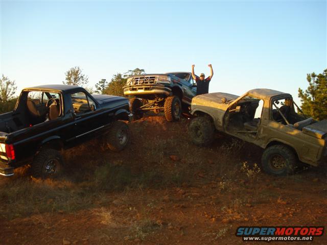 Three off-road trucks on a dirt hill, one with a person celebrating