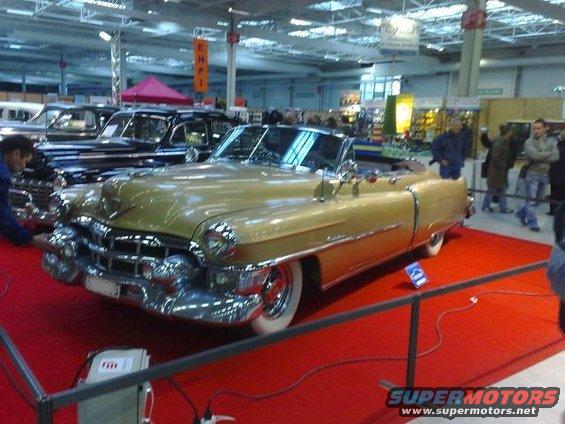 Gold 1953 Cadillac convertible on display with other cars behind it