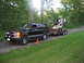 1998 Chevrolet Tahoe - A black 1998 Chevrolet Tahoe tows a trailer carrying a skid steer loader on a wooded dirt road.