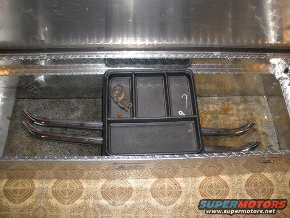 Truck bed toolbox with a black organizer tray, two chrome pipes, and some small hardware