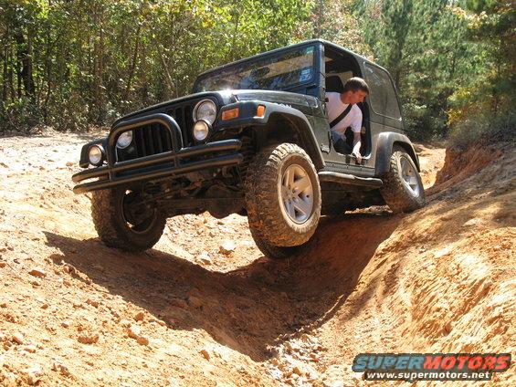 Black Jeep Wrangler climbing out of a deep rut on a rocky off-road trail