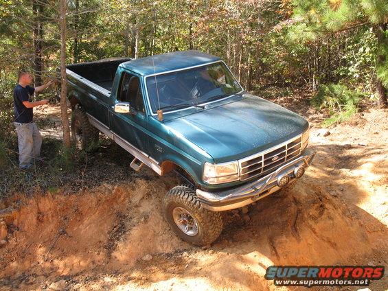Green lifted Ford F-250 pickup descending a steep dirt embankment in the woods