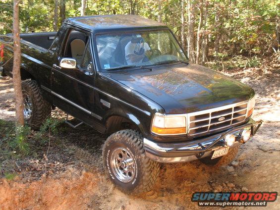 Black lifted Ford pickup truck with light bar climbing a dirt trail in the woods