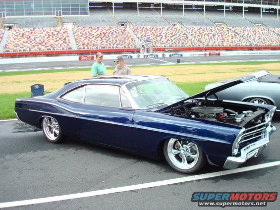 dark blue coupe with hood open, parked next to another car at a racetrack