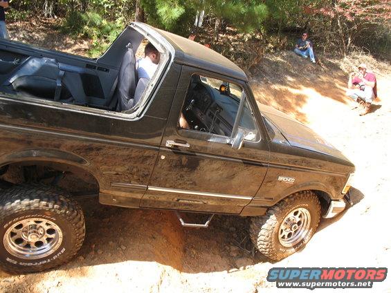 Black lifted 1990s Ford Bronco with top removed climbing a dirt embankment