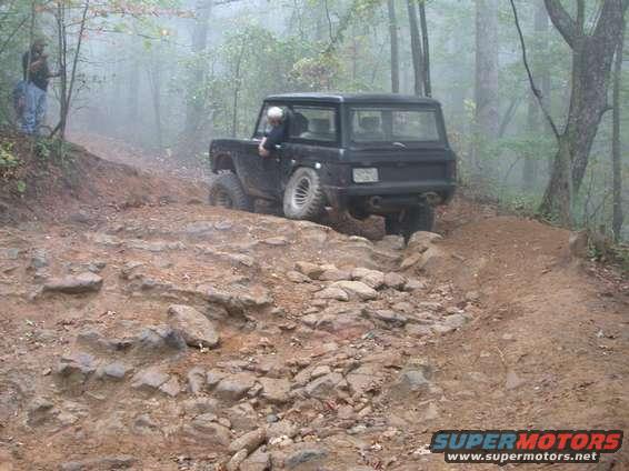 1972 Ford Bronco driving on a rocky, wooded trail