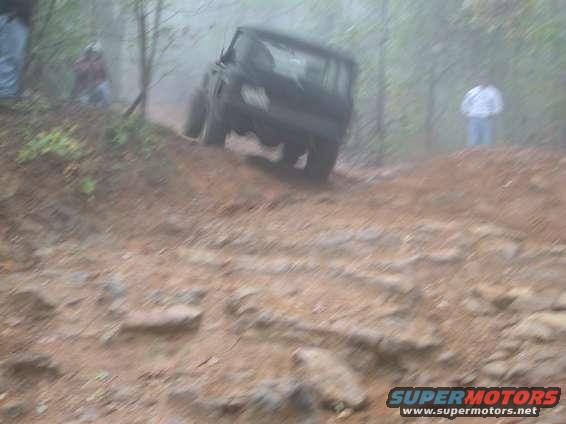 Black SUV driving up a rocky, muddy hill in a forest