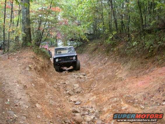 Black SUV navigating a rocky, muddy trail in a wooded area