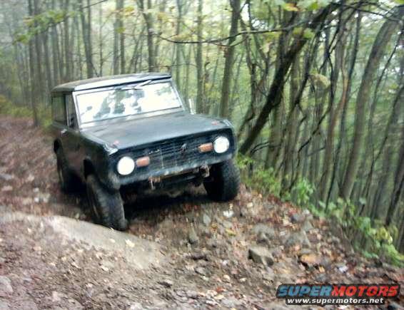 1972 Ford Bronco driving on a dirt path in a forest