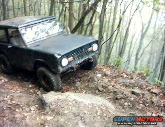 Dark colored Ford Bronco climbing a rocky, wooded trail