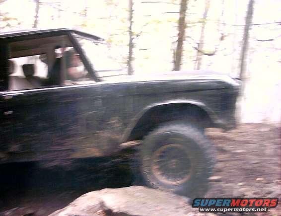 Black Ford Bronco driving off-road, side view, showing front fender and wheel