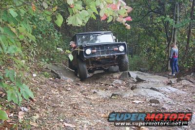 Black 1970 Ford Bronco navigating a rocky trail with a person driving and another watching