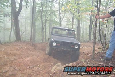 1972 Ford Bronco driving on a muddy, wooded trail