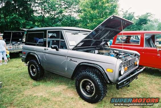 1972 Ford Bronco with hood open, parked on grass next to a red vehicle