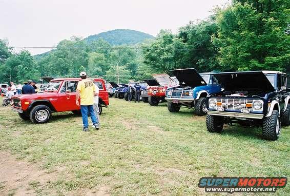 Several Ford Broncos parked on grass, some with hoods up. One red Bronco is in the foreground with a person wearing a yellow 'STAFF' shirt