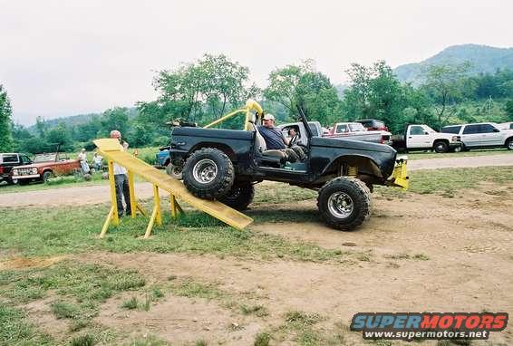 Black Ford Bronco with roll cage on a wooden ramp, front wheels elevated