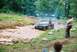1972 Ford Bronco - A Jeep CJ-5 is stuck in a mud pit with a person watching from the side.