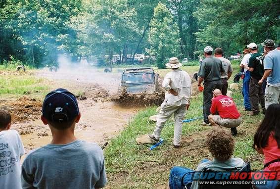 Off-road vehicle splashing mud, front view, with spectators watching