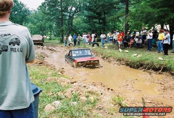 Red 1972 Ford Bronco stuck in a mud pit with a crowd watching
