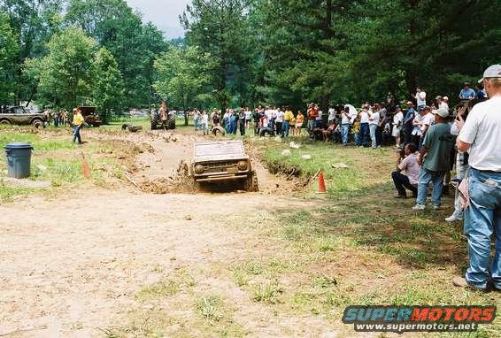 Jeep CJ-5 driving through mud pit with spectators watching