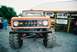 1972 Ford Bronco - A lifted 1972 Ford Bronco with oversized tires is parked in front of a building with various signs.