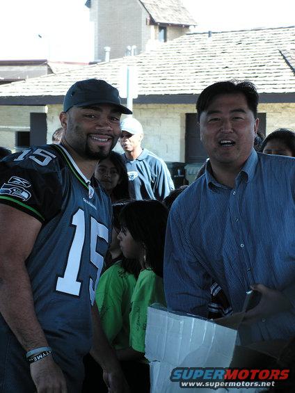Man in Seahawks jersey and another man smile at the camera, with people behind them