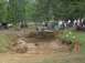 1972 Ford Bronco - A crowd watches as a modified off-road vehicle navigates a deep mud pit, kicking up a large spray.