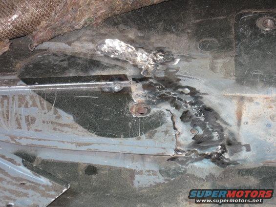 Welded floor pan repair with visible metal patches and bolts
