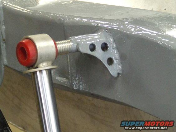 Close-up of a red and silver shock absorber mount attached to a gray painted vehicle frame